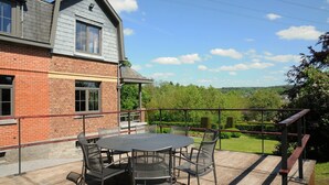Une terrasse avec une table ronde et des chaises, un bâtiment en briques et une vue sur un paysage verdoyant.