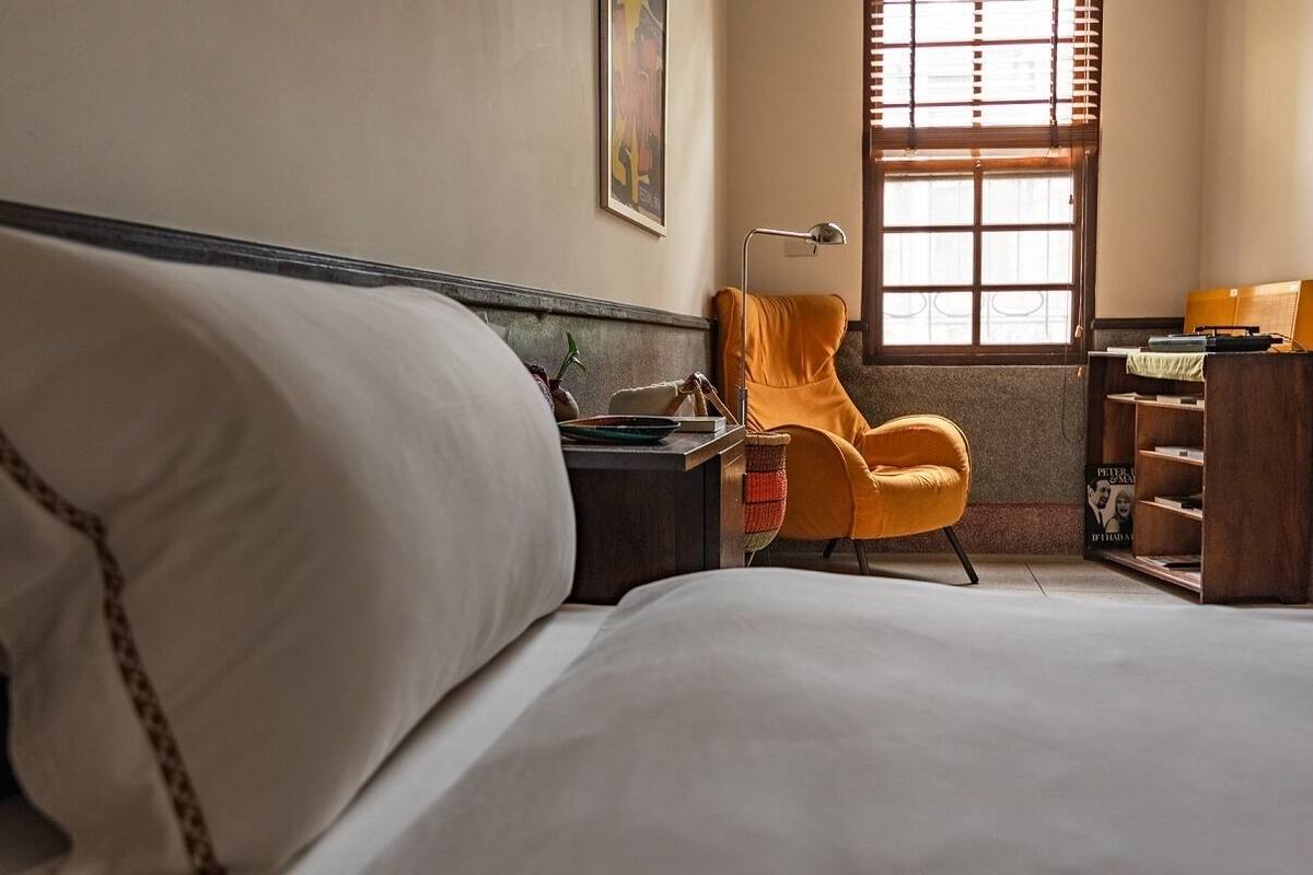 A hotel room with a bed, a desk with a lamp, a chair, and a window with blinds.