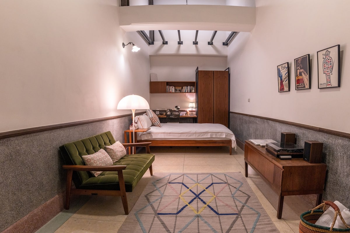 A cozy bedroom with a bed, a green sofa, a wooden desk, and a bookshelf.