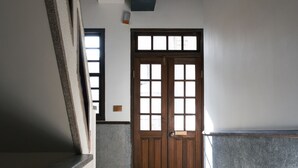A corridor with a wooden door, a vent on the ceiling, and a tiled floor. - Originn (Taipei)