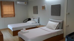 Een hotelkamer met twee eenpersoonsbedden, een houten nachtkastje, een wandairconditioner en drie ingelijste kunstwerken.