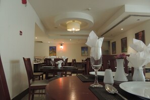 A dining area with tables set for two, featuring white plates, silverware, and clear glassware. - President hotel (Amman)