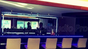 Zona de bar con cuatro sillas blancas, una barra con espejo y un ventanal con vista a un edificio.