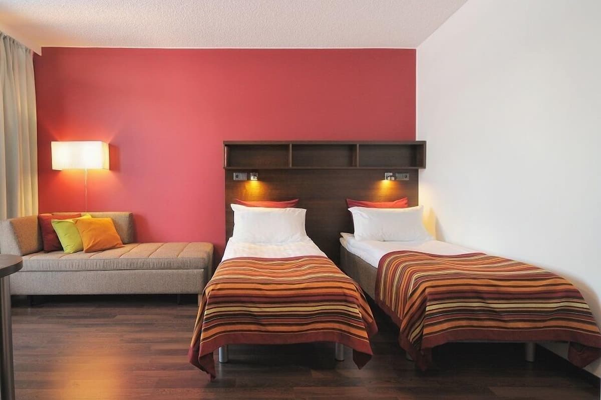 Een hotelkamer met twee éénpersoonsbedden, een bank en een nachtkastje.