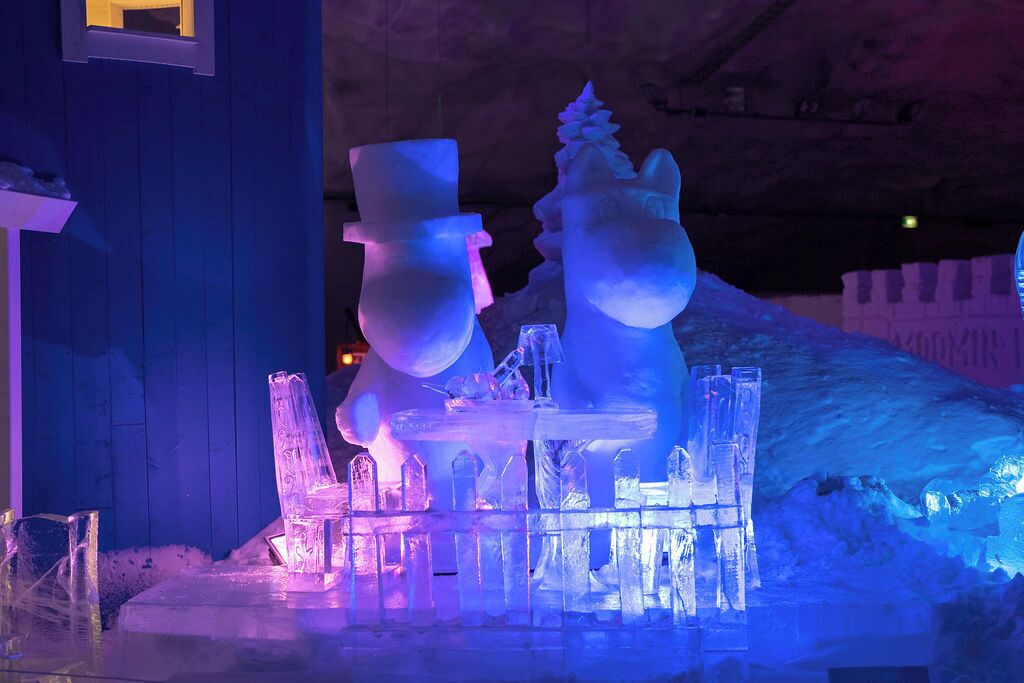 Una exhibición de esculturas de nieve con diversas figuras y estructuras, incluyendo una figura con bombín y un muñeco de nieve.