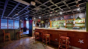 Un espace bar avec des tabourets en bois, un comptoir où sont exposées des bouteilles et une vue dégagée grâce à de grandes fenêtres.