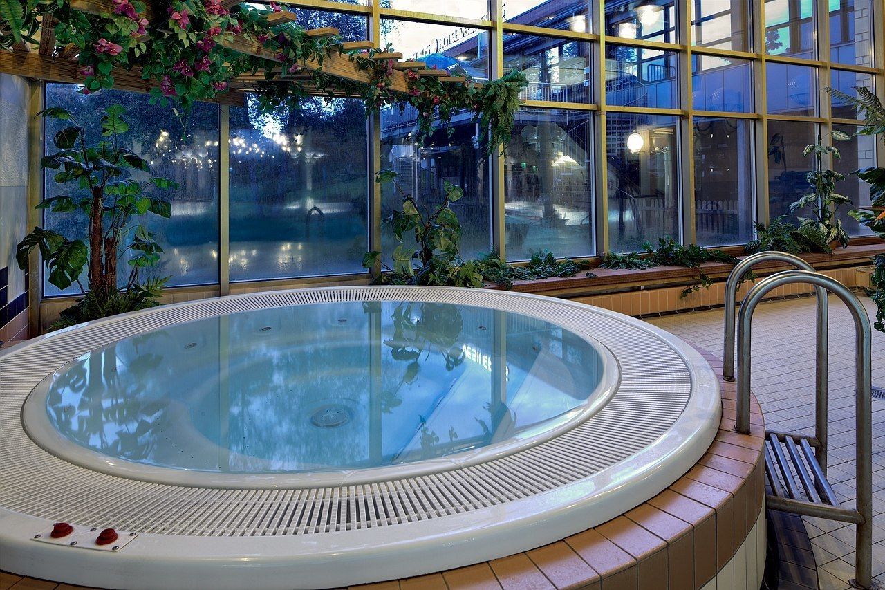 Jacuzzi con cerramiento de vidrio, rodeado de plantas y vistas a un edificio a través de amplios ventanales.