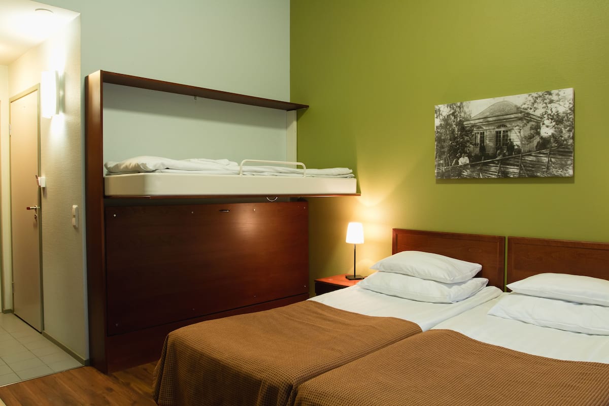 Een hotelkamer met een stapelbed, een enkel bed, een nachtkastje met een lamp en een aan de muur bevestigd schilderij.