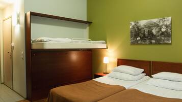 Habitación de hotel con literas, una cama individual, una mesita de noche con lámpara y un cuadro colgado en la pared.