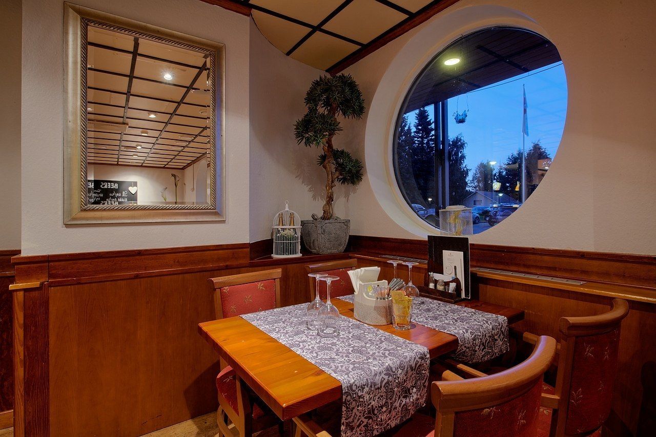 Un restaurante con mobiliario de madera, un ventanal grande y una planta en maceta.