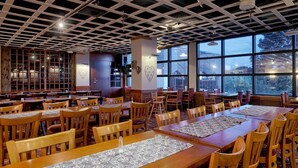 Un vaste espace dédié à la salle à manger, avec des tables et des chaises en bois, de grandes fenêtres donnant sur l’extérieur et un plafond orné d’un motif en réseau.