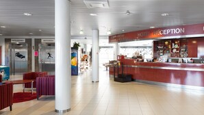 Un hall d'hôtel comprenant un comptoir d'accueil, un espace salon avec des fauteuils rouges et deux ascenseurs portant les inscriptions « HOTELLIHUONEET » et « HIHTOAREENA ».