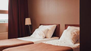 Habitación de hotel con dos camas individuales, una mesita de noche con lámpara y una ventana con cortinas.