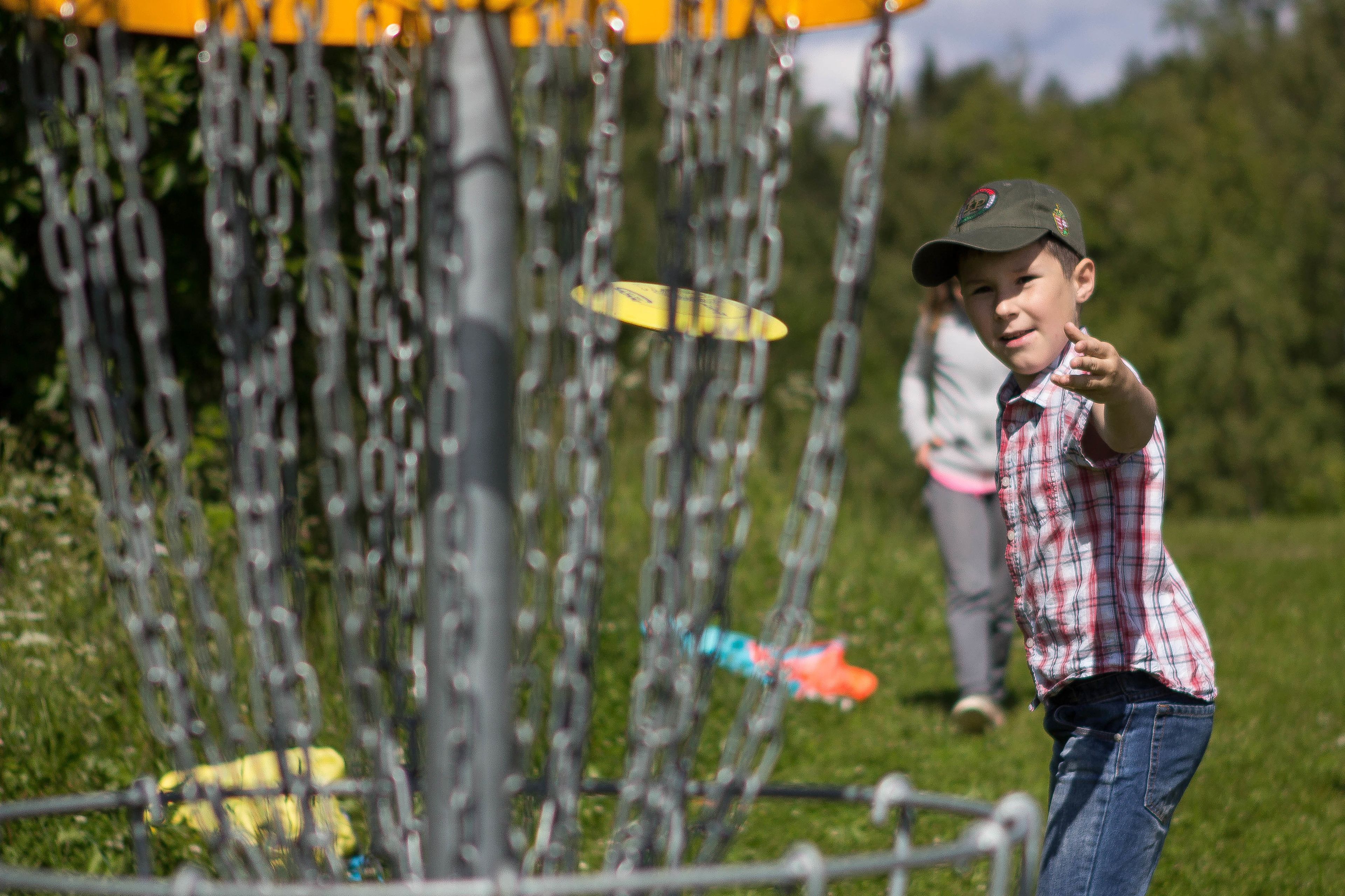 A person playing with a frisbee in an outdoor area with a chain-link fence and greenery in the background.