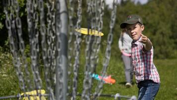 A person playing with a frisbee in an outdoor area with a chain-link fence and greenery in the background.