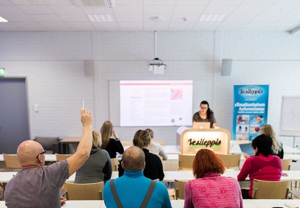 Un aula con una pantalla de presentación, un atril y asistentes.