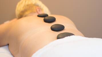 A person receiving a back massage with black stones placed on their back.