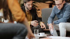 Un groupe de personnes est réuni autour d’une table, avec une tasse de café et un ordinateur portable.