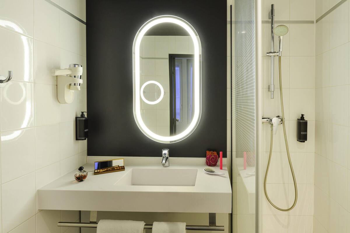 Un baño moderno con un espejo grande, una ducha y un lavamanos.