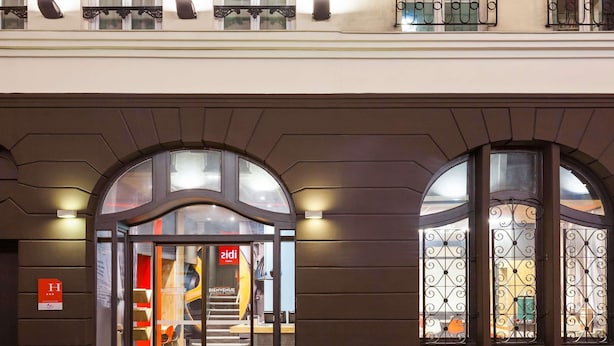 L’entrée d’un hôtel, avec une porte en verre, un escalier menant à l’intérieur et un balcon à l’étage.