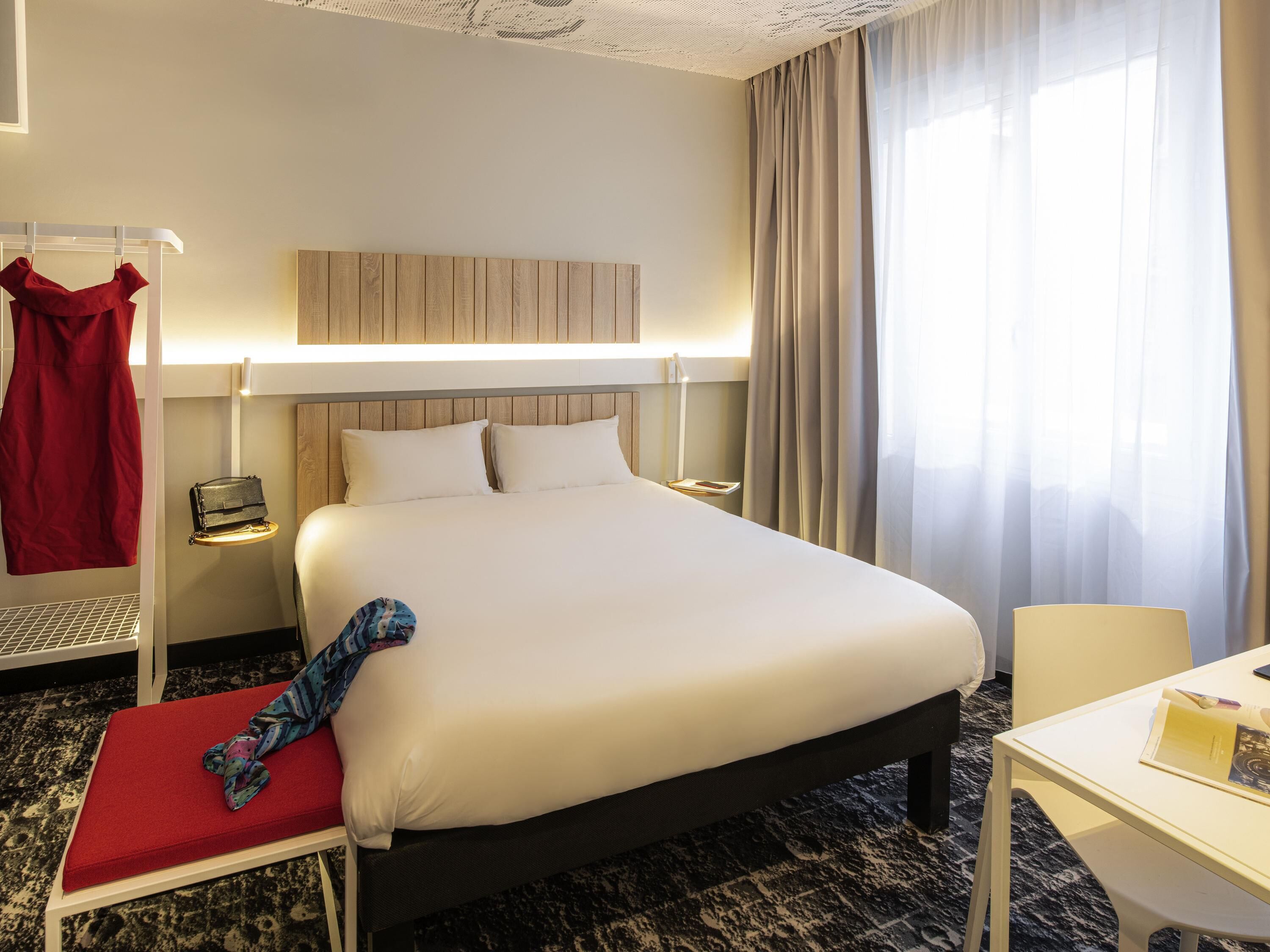 Habitación de hotel con una cama grande, mesitas de noche, un escritorio y un vestido rojo colgado en un perchero.
