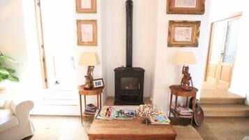 Uma sala de estar aconchegante com uma lareira a lenha, quadros nas paredes, uma mesa de centro com revistas e um violão encostado na parede.