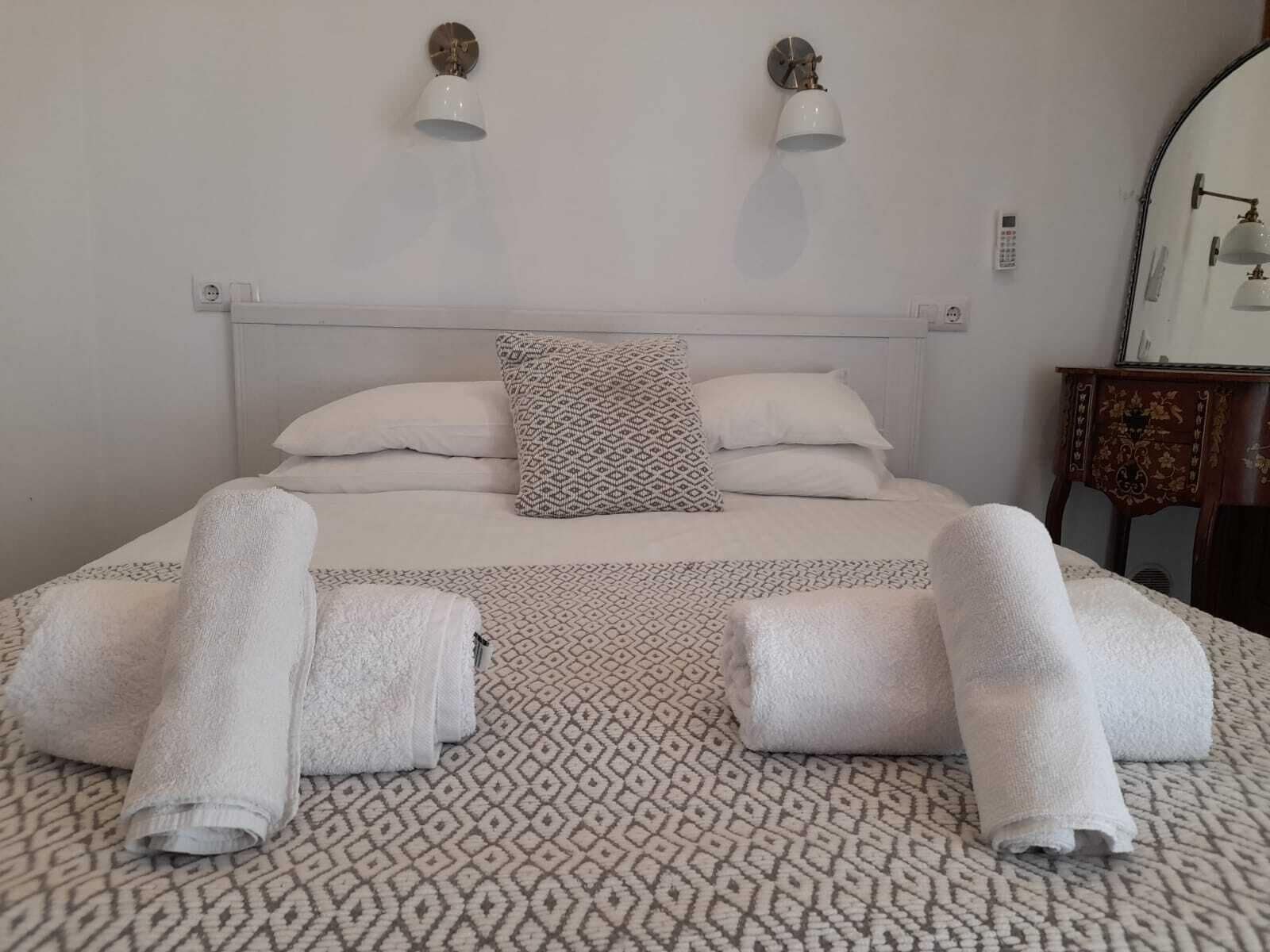 A neatly made bed with a patterned bedspread, two wall-mounted lamps, and a bedside table with a mirror.