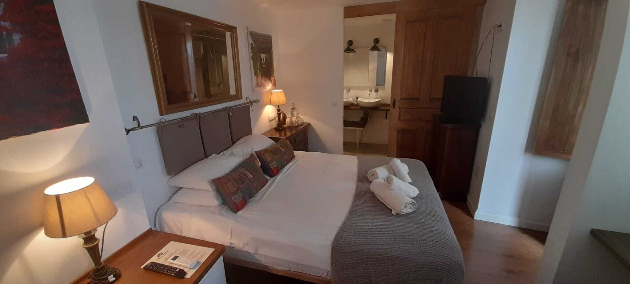Ein Hotelzimmer mit einem Bett, einem Nachttisch mit Lampe, einem Spiegel, einem Badezimmer mit Waschbecken und Spiegel sowie einem Fernseher.