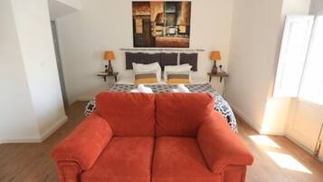 Quarto com cama, sofá vermelho, duas mesas de cabeceira com abajures e um quadro na parede.