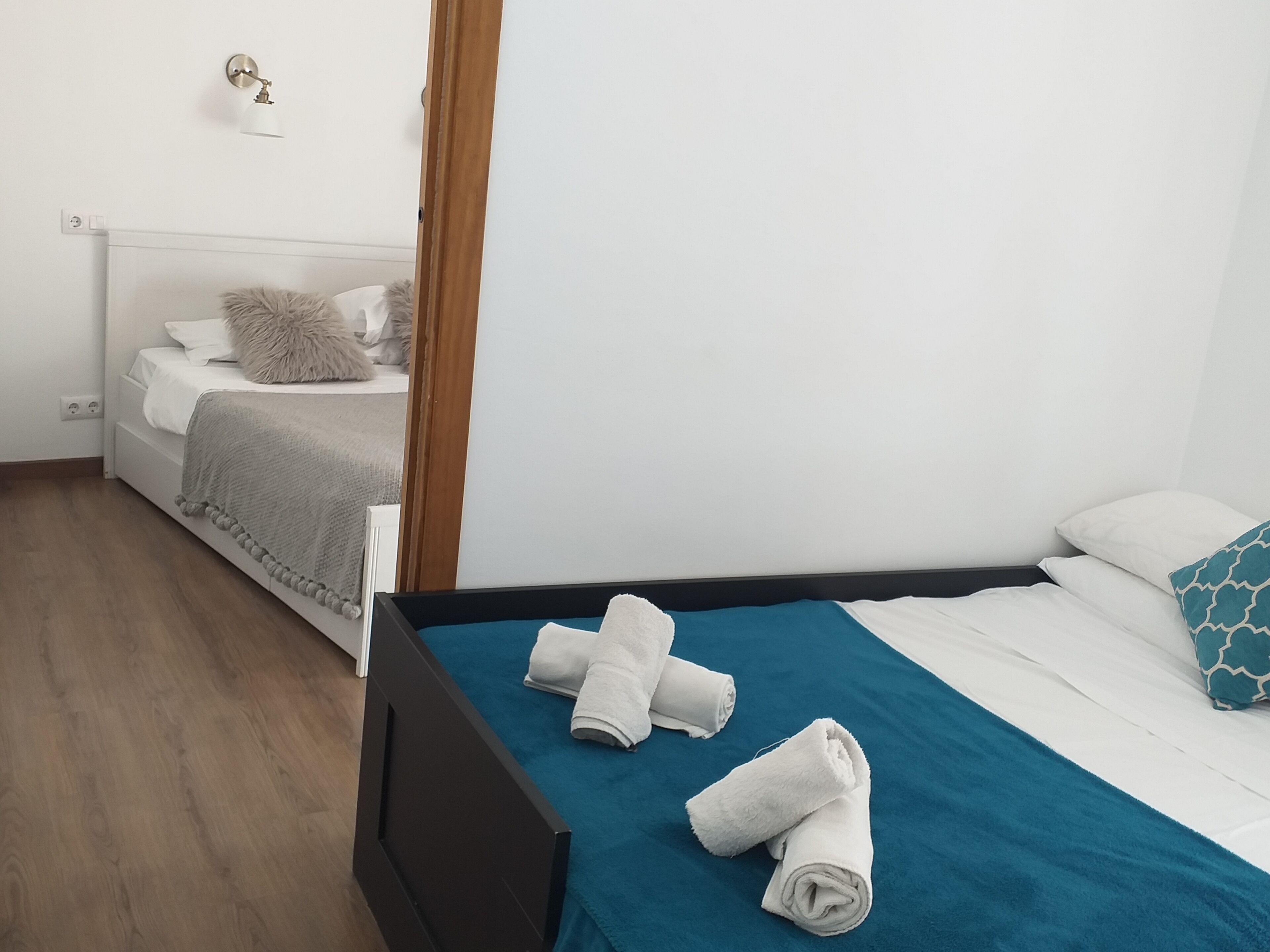 A bedroom with a bed, a blue bedspread, and two rolled towels on the bed.