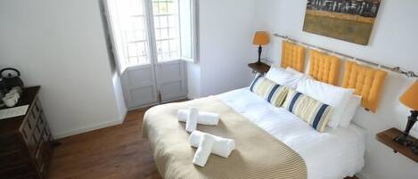 A bedroom with a bed, a window, a painting, and a nightstand.