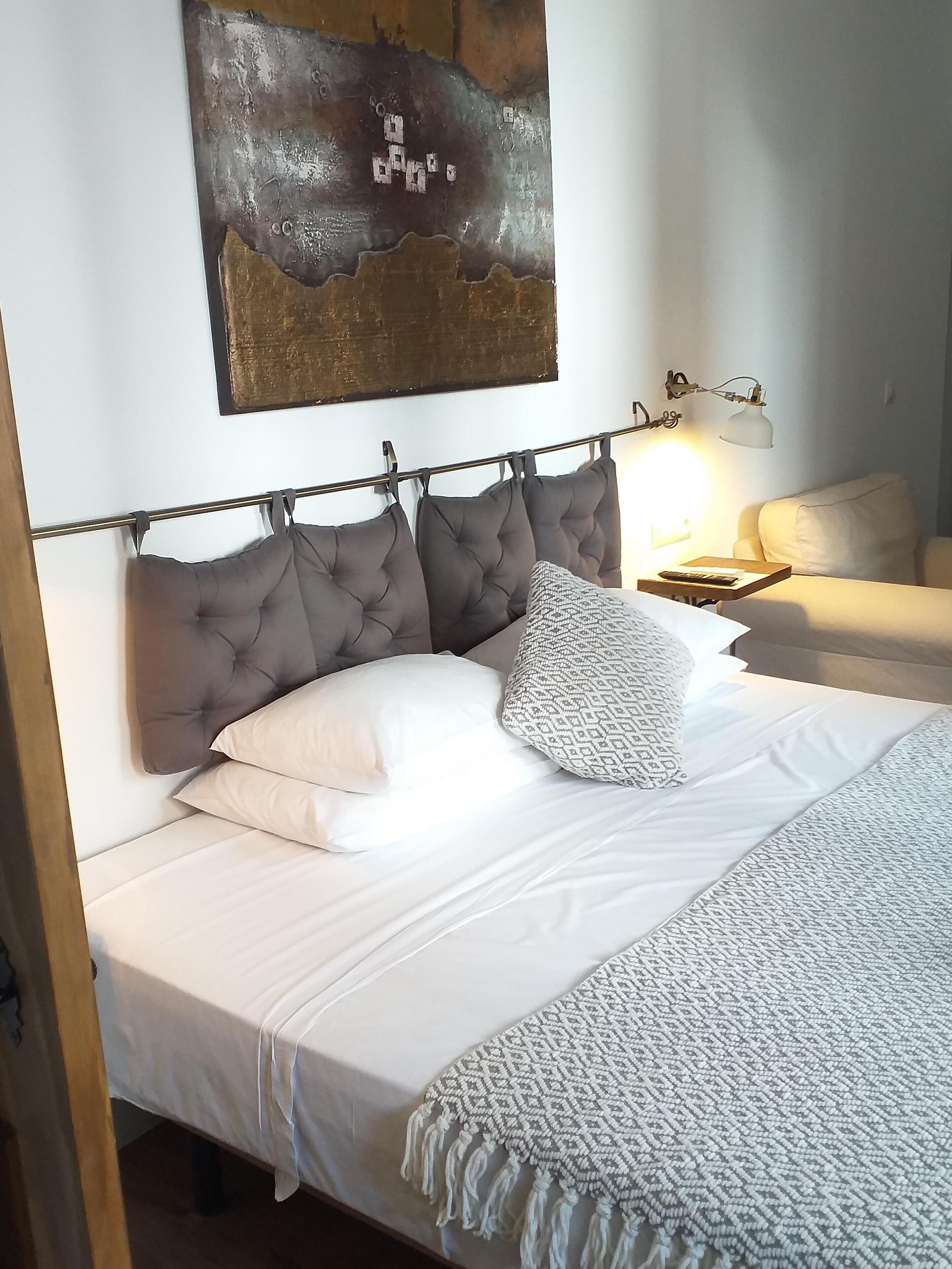 Una cama bien hecha con cabecera gris, ropa de cama blanca y una manta decorativa.