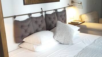 Una cama bien hecha con cabecera gris, ropa de cama blanca y una manta decorativa.