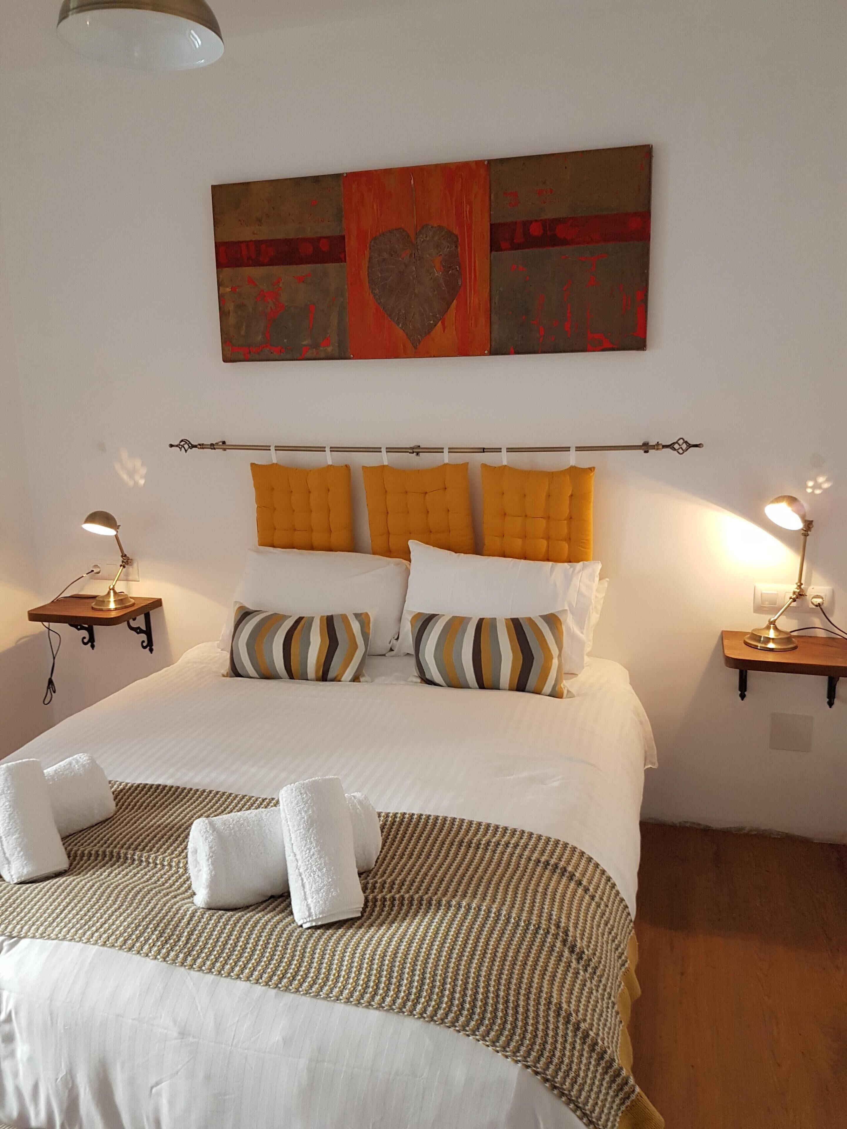 A neatly made bed with a striped blanket, two bedside lamps, and a wall art piece above it.