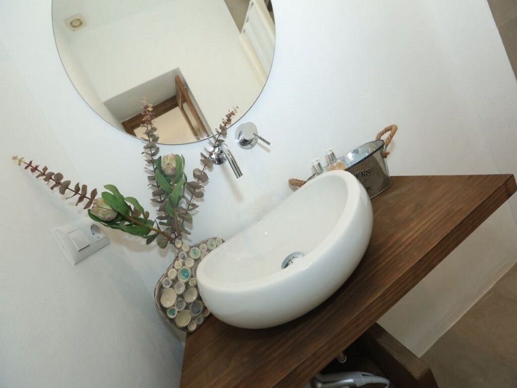 Une salle de bain avec un lavabo blanc, un miroir rond et un meuble-lavabo en bois.