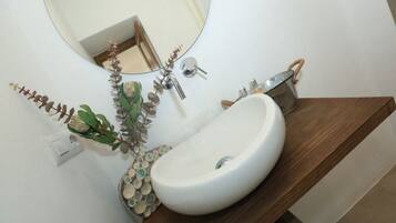 Une salle de bain avec un lavabo blanc, un miroir rond et un meuble-lavabo en bois.