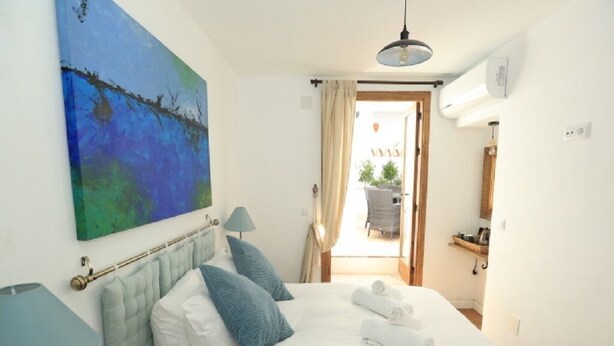 A hotel room with a bed, a painting, a lamp, and a view of the outside. - Millers of Frigiliana (Frigiliana)