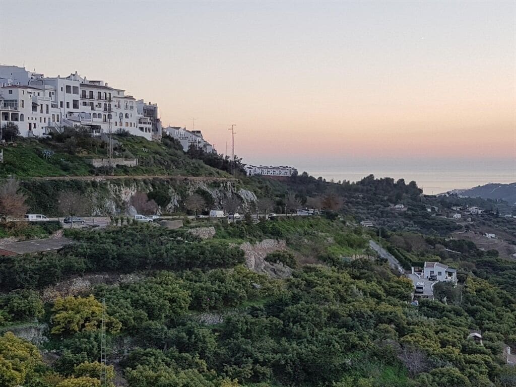 Une ville côtière avec des bâtiments blancs construits sur une colline, un ciel dégagé et une vue sur la mer.