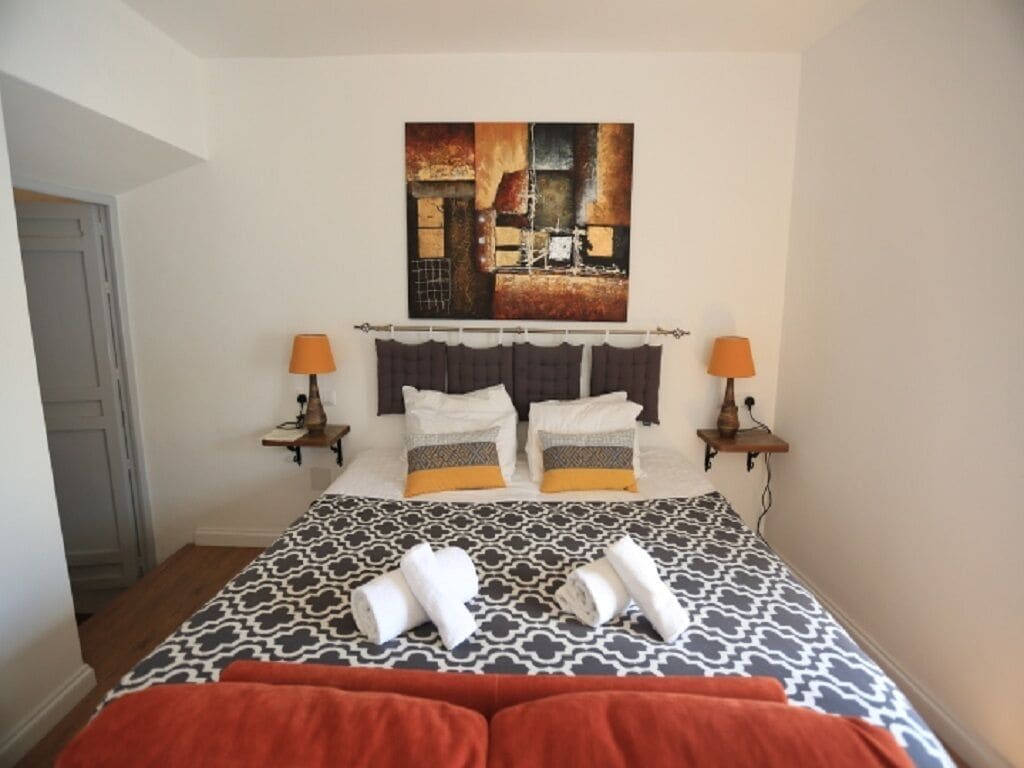Habitación de hotel con una cama grande, dos mesitas de noche, un cabecero y un cuadro en la pared.