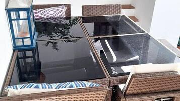 Un comedor con una mesa de vidrio, sillas de mimbre y un farol.