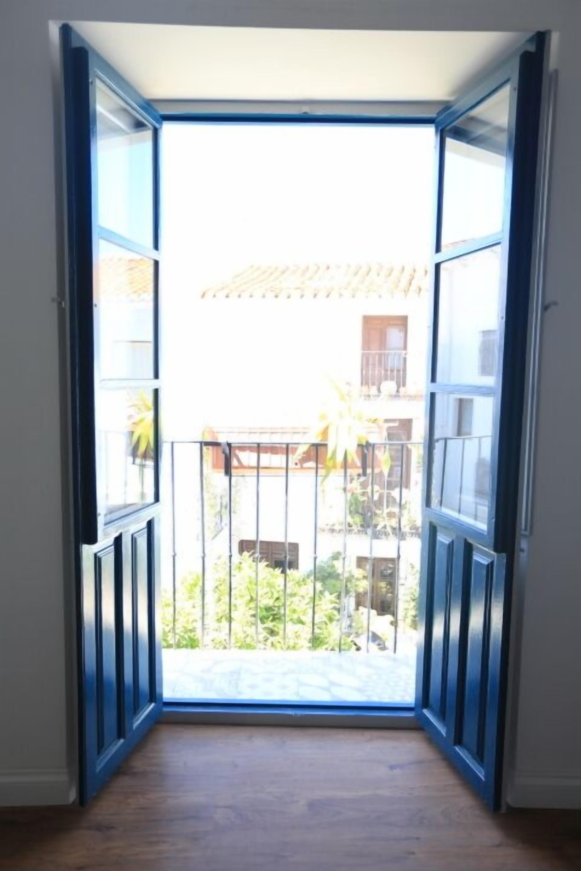 Una porta oberta que dona a un balcó amb vista a un edifici i algunes plantes.