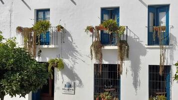 Un edificio blanco con contraventanas azules y numerosas ventanas, algunas con plantas colgantes.