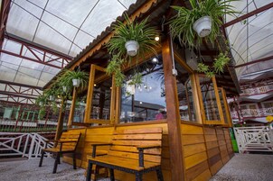 A wooden structure with hanging planters, benches, and a glass enclosure.