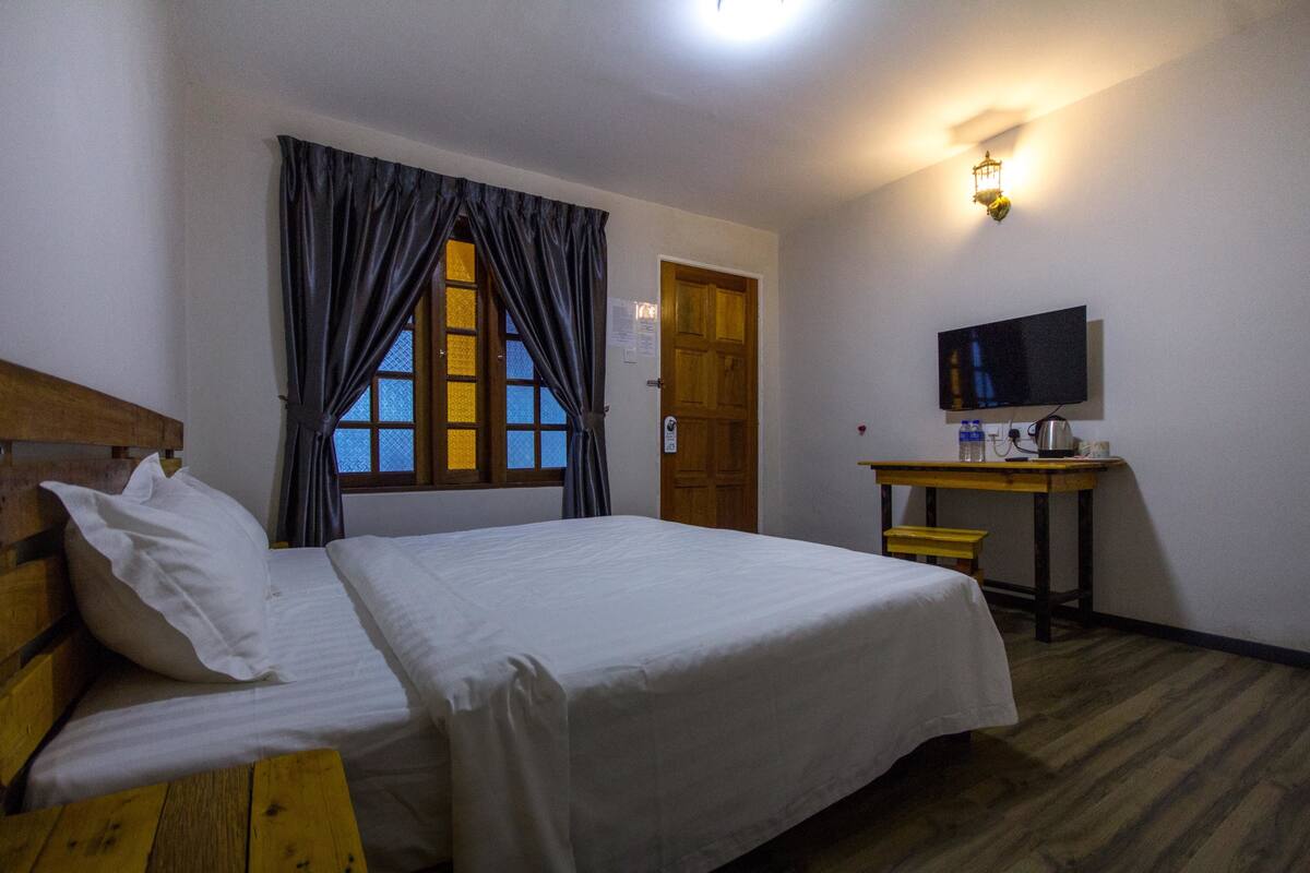 Una habitación con cama, un escritorio de madera, televisor y ventana con cortinas.