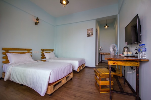 A room with two wooden beds, a wooden desk, a television, and a fan.