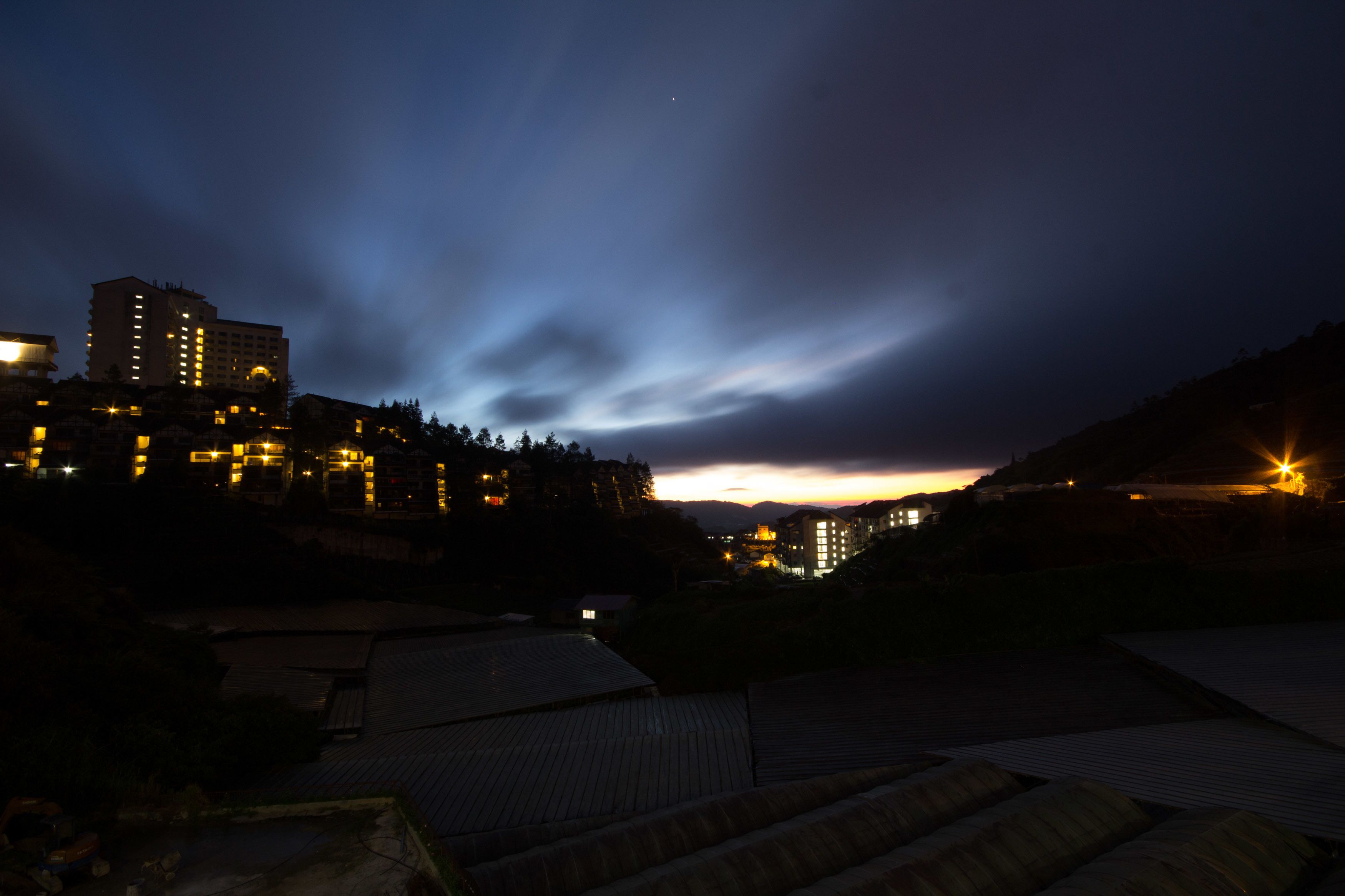 A nighttime view of a cityscape with illuminated buildings and a cloudy sky.