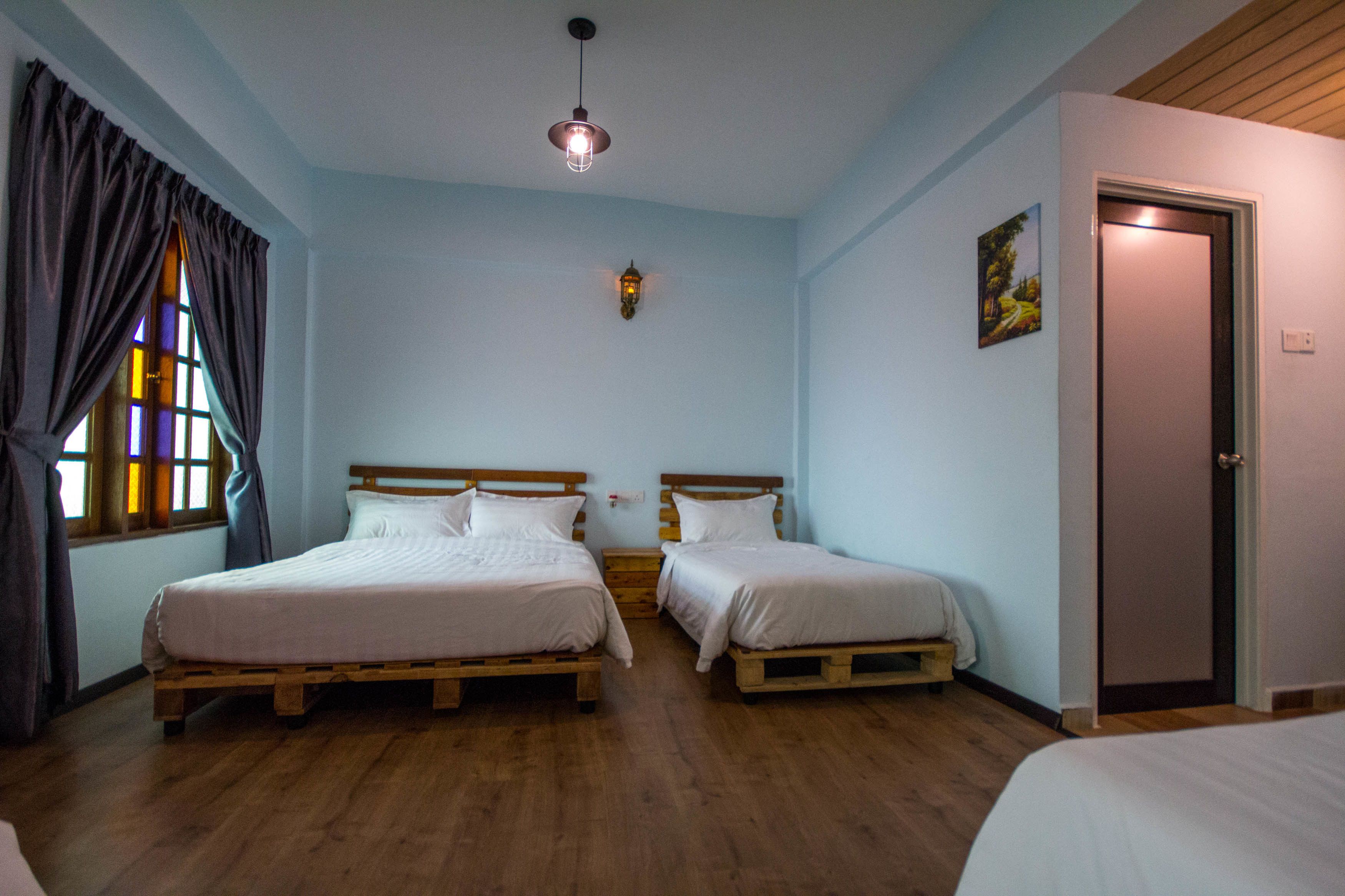 A room with two wooden beds, a wooden ceiling, a wall-mounted light fixture, and a door.