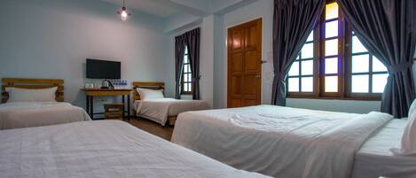 A hotel room with three beds, a television on a desk, and a window with curtains.