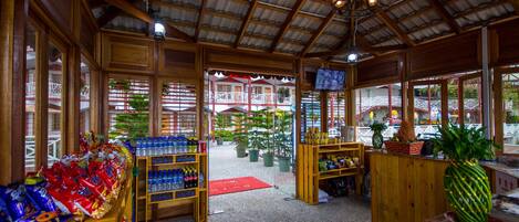 A spacious lobby with wooden furniture, a TV mounted on the wall, and a view of the outdoor area with plants and a red carpet.