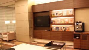 A modern hotel room with a flat-screen TV, a coffee machine, and a bookshelf with books and magazines. - JR East Hotel Mets Niigata (Niigata)